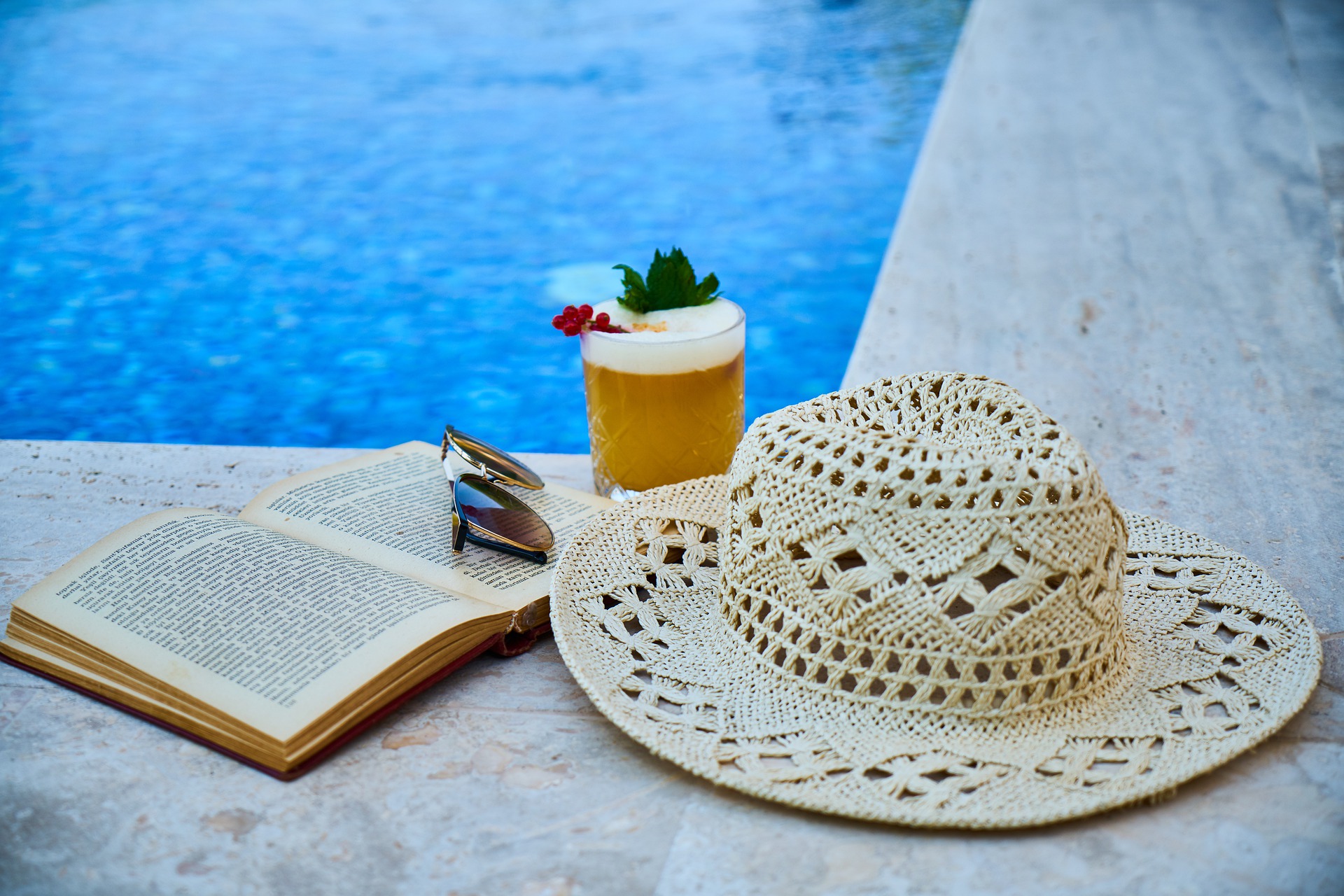 Symbolbild mit Buch, Hut und Drink am Pool