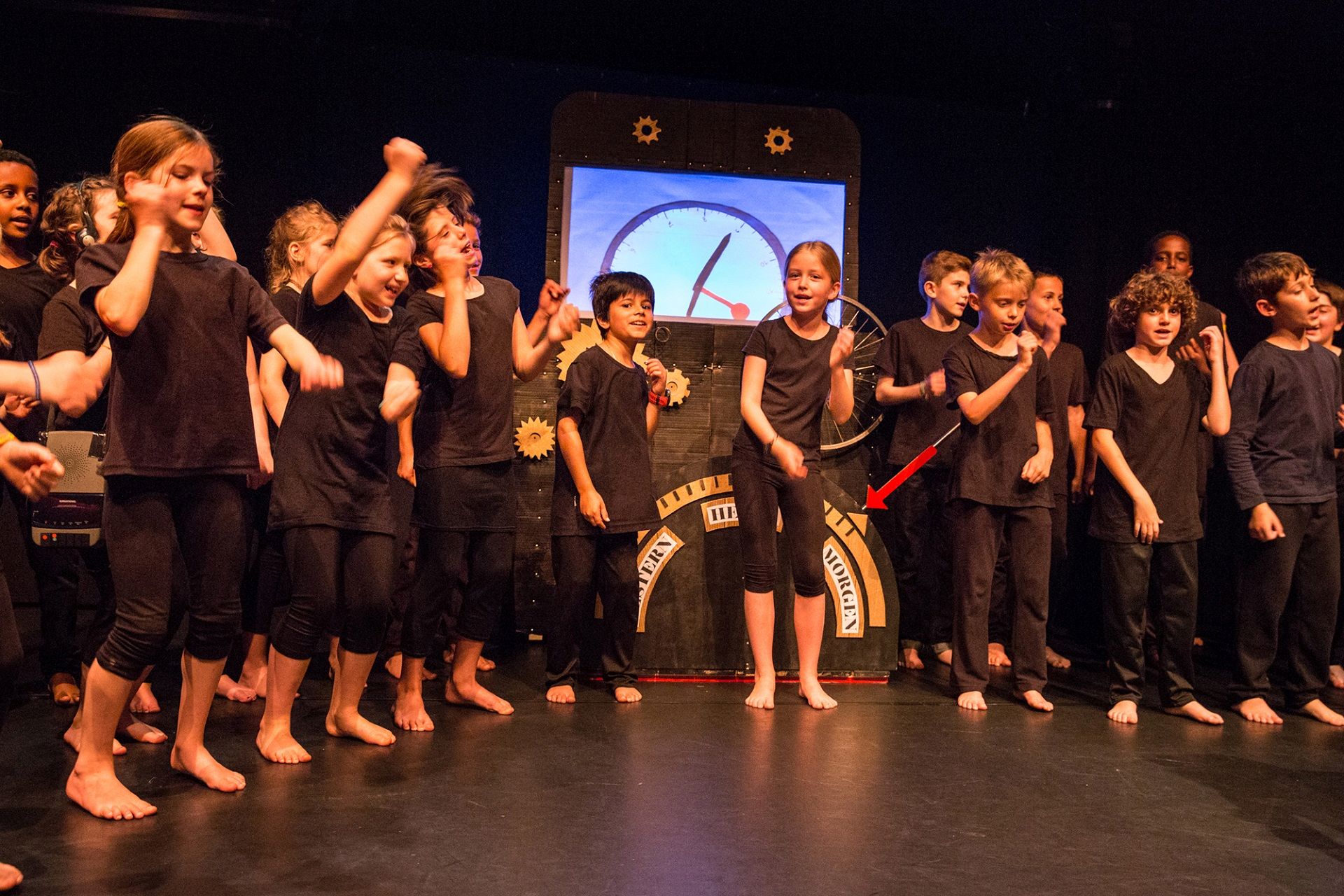 Kinder tanzen schwarz gekleidet auf einer Bühne und haben Spass