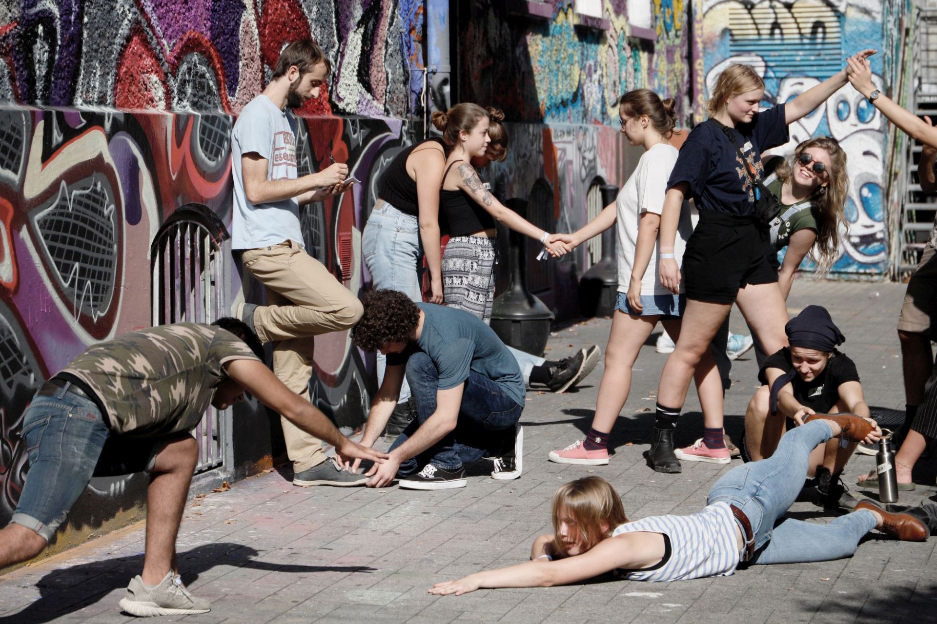 Jugendliche stehen und sitzen in unterschiedlichen Posen vor eine Graffiti-Wand 