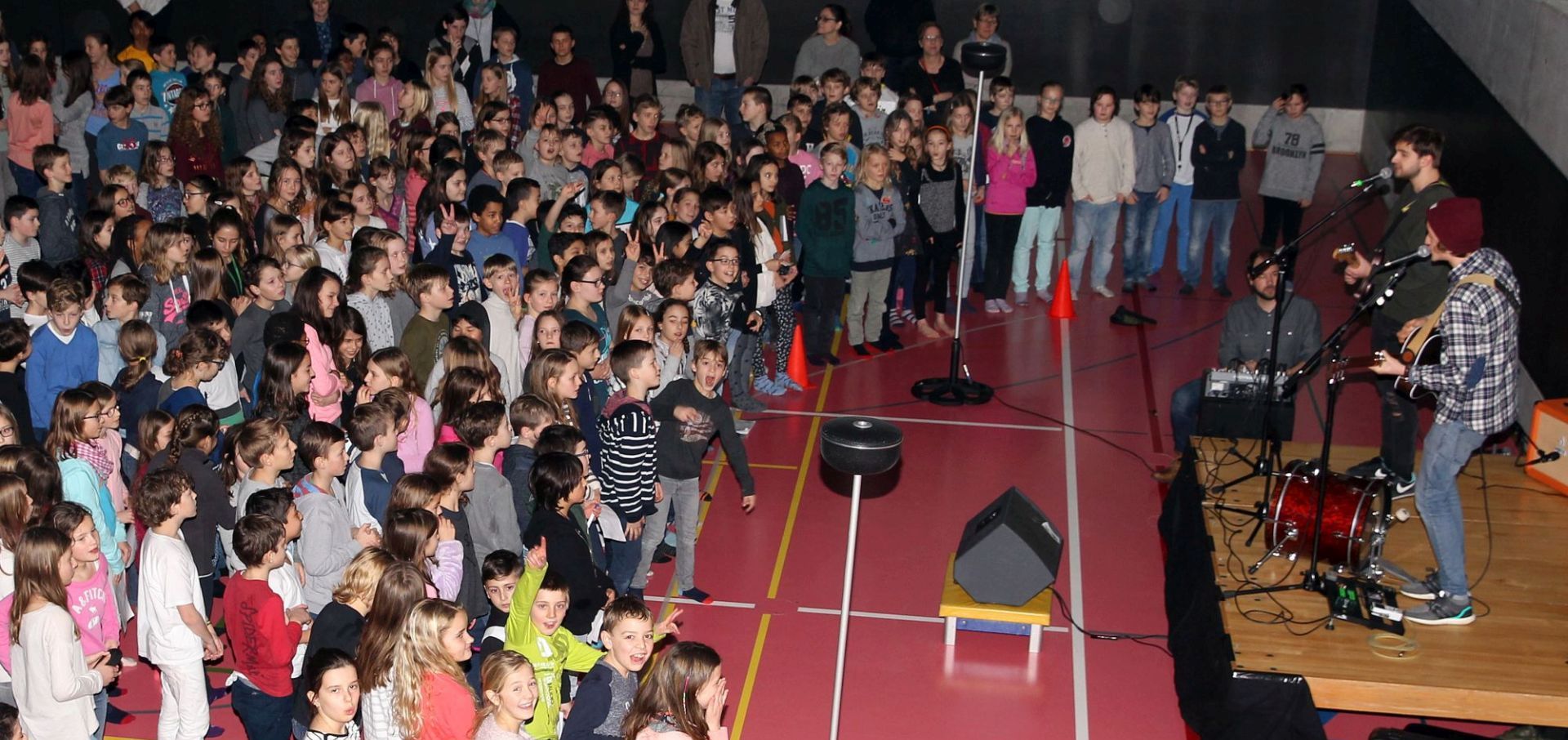 Schülerinnen und Schüler tanzen in einer Turnhalle, auf einer Bühne spielt eine Band