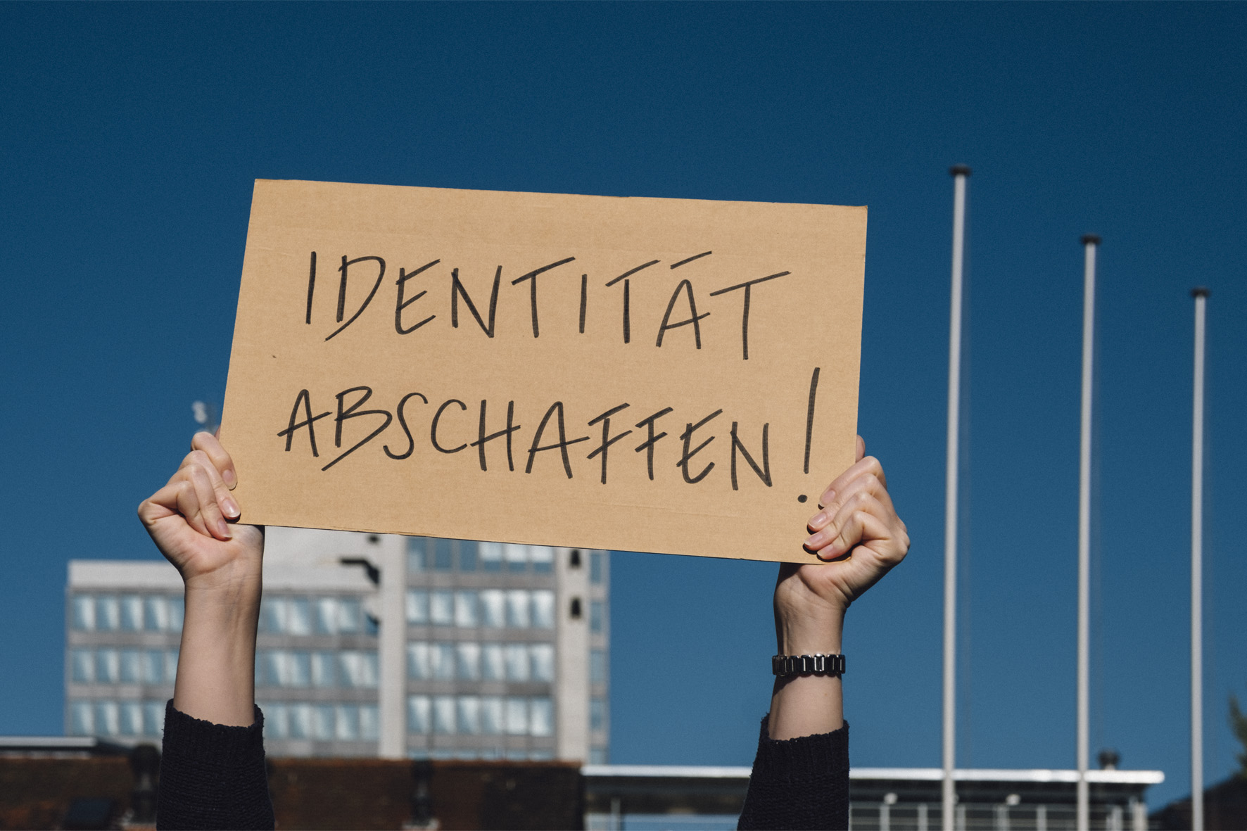 Symbolbild mit Person, die Schild mit dem Text "Identität abschaffen" hochhält.